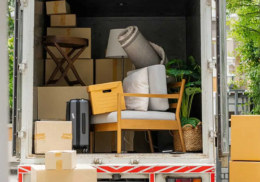 Impresa di pulizie Antonella Sgombero locali Sgombero Cantine, Solai, Garage. Camion di fronte alla porta di entrata di una casa con il retro aperto e riempito di svariati oggetti come sedie, tappeti valigie e scatoloni