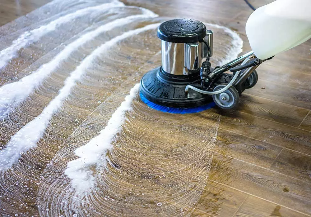 Impresa di pulizie AntonellaTrattamento superfici in marmo, legno, pietra. Macchinario con spazzola blu in primo piano che sta trattando un apvimento in legno