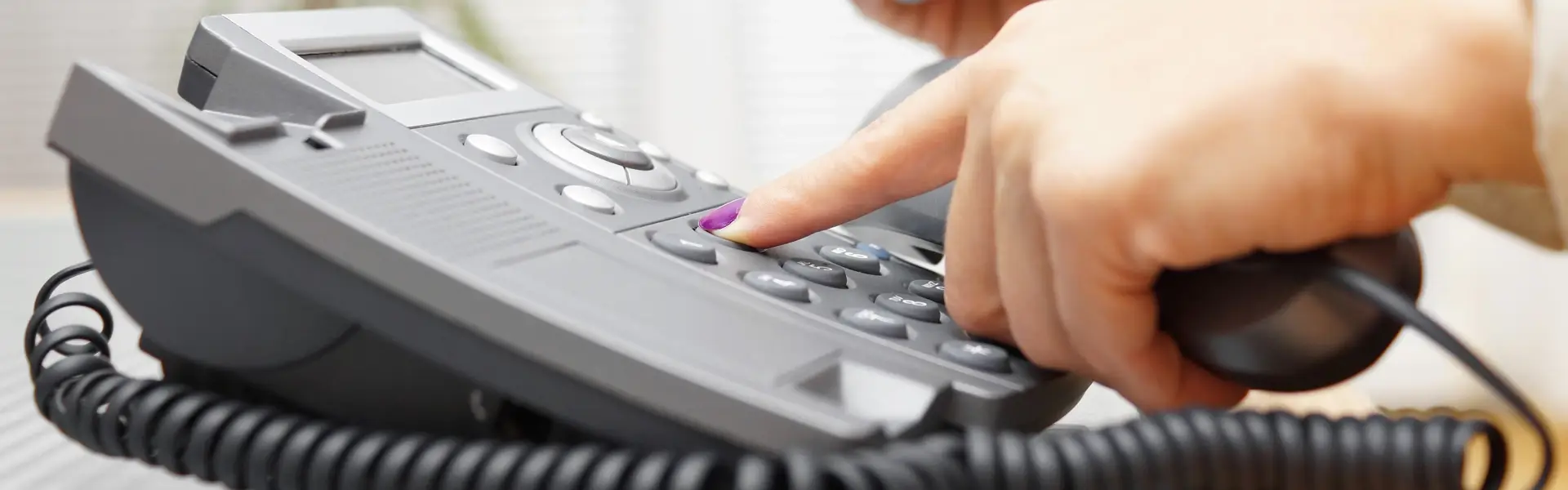 Impresa di Pulizie Antonella Contatti. Primo piano della mano con unghia viola di una ragazza che compone il numero su un telefono fisso
